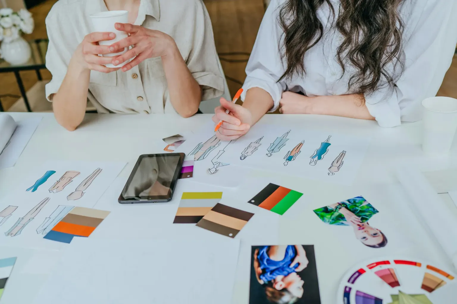 Two people reviewing fashion sketches and color samples on a table