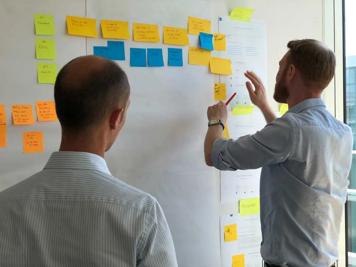 Two workshop participants arranging sticky notes and reviewing printed materials on a wall