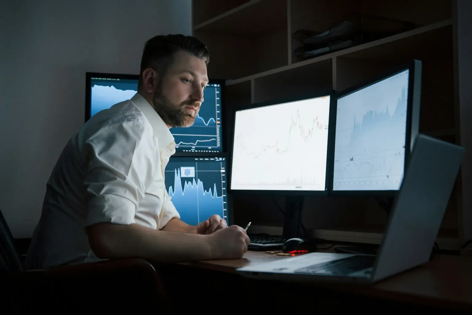 Man seated at a desk with charts displayed across multiple computer screens