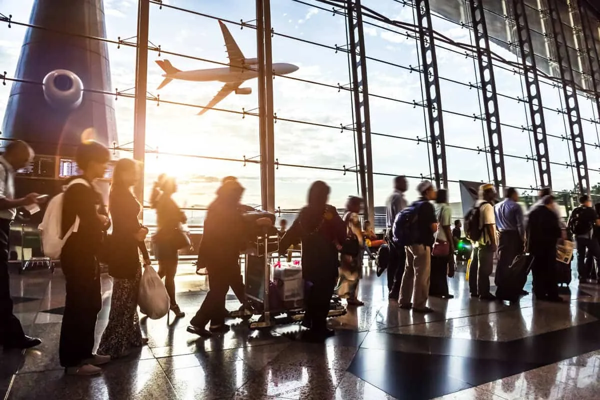 Travelers waiting inside an airport as a plane passes the terminal windows