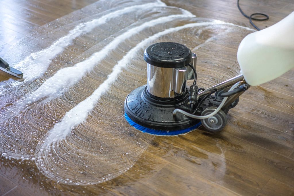 Commercial floor-cleaning machine scrubbing a wood floor