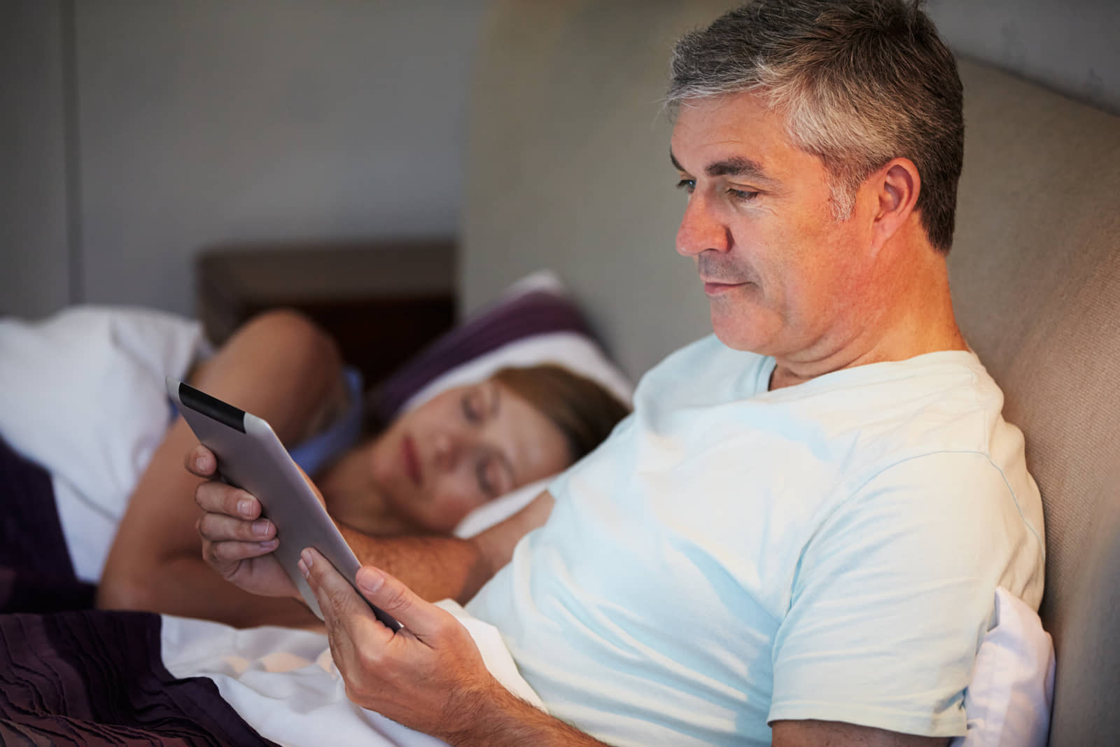 Man reading from a tablet while reclining in bed